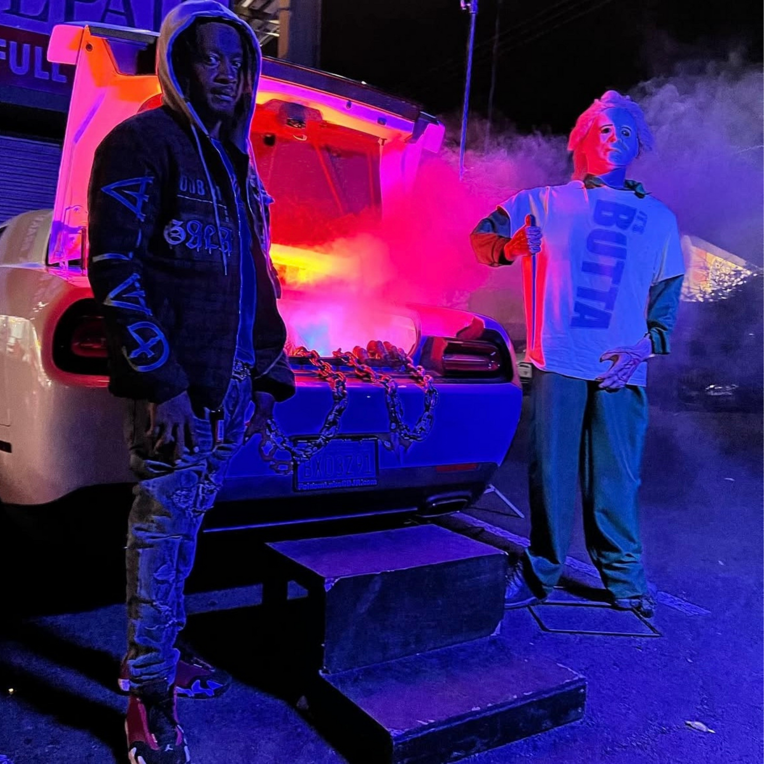 our founder standing next to a car decorated for Halloween with colorful lighting effects and a Jason themed mannequin in the background.